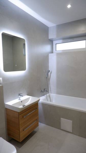 A bathroom with a bathtub and a sink, complemented by a backlit mirror in a family house.