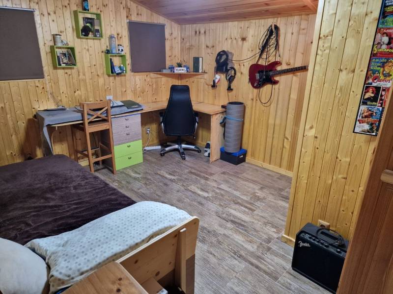 A room with wooden walls, a floor with a wooden decor, a desk, and a guitar on the wall.
