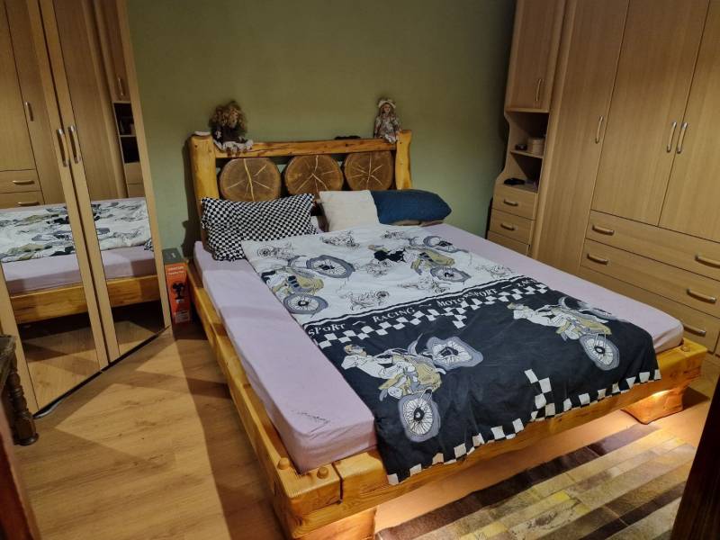 A bedroom in a family house with a wooden bed, built-in wardrobes, and a floor with a wooden decor.