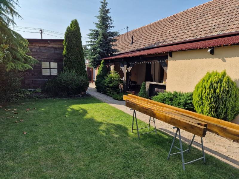 A family house in Dlhá nad Váhom with a lawn, bushes, and a wooden bench in the garden.