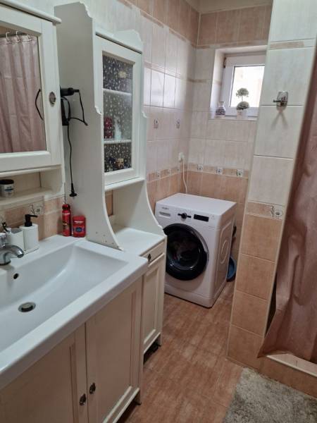 A bathroom in a family house with a sink, washing machine, and cabinet in neutral shades.