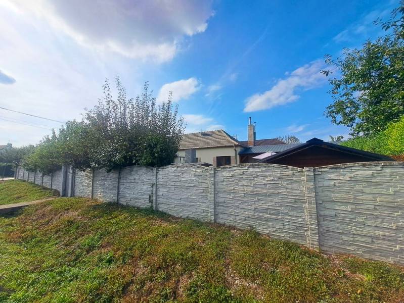 A family house in Neded with a stone fence and a landscaped garden under a blue sky.
