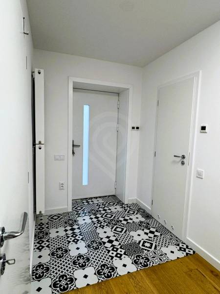 A hallway in a family house with tiled flooring and patterned decor, white walls, doors.
