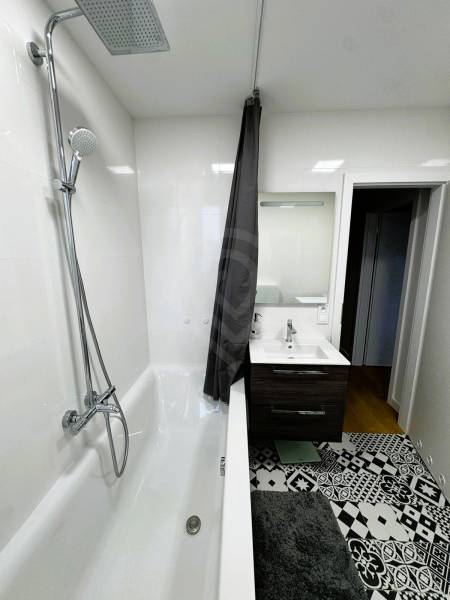 Bathroom with a bathtub, shower, sink, and patterned tiles in a family house.
