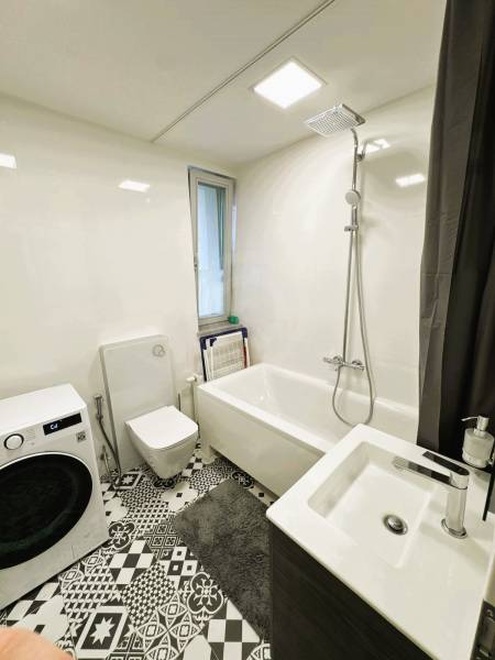 A bathroom in a family house with a bathtub, washing machine, and black-and-white floor with a geometric pattern.