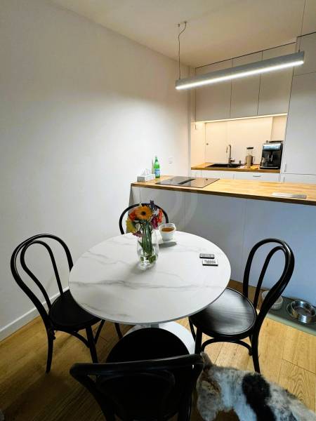 Dining room in a family house with a round table, flowers, and a wooden-patterned floor.