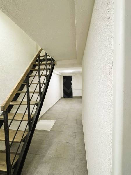 A hallway of a family house with minimalist stairs, light walls, and tiles.
