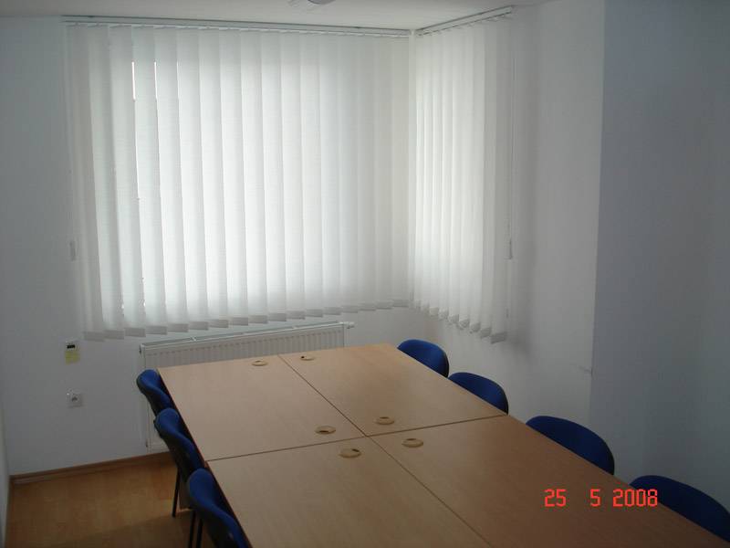 Commercial space with a conference table, blue chairs, and vertical blinds.