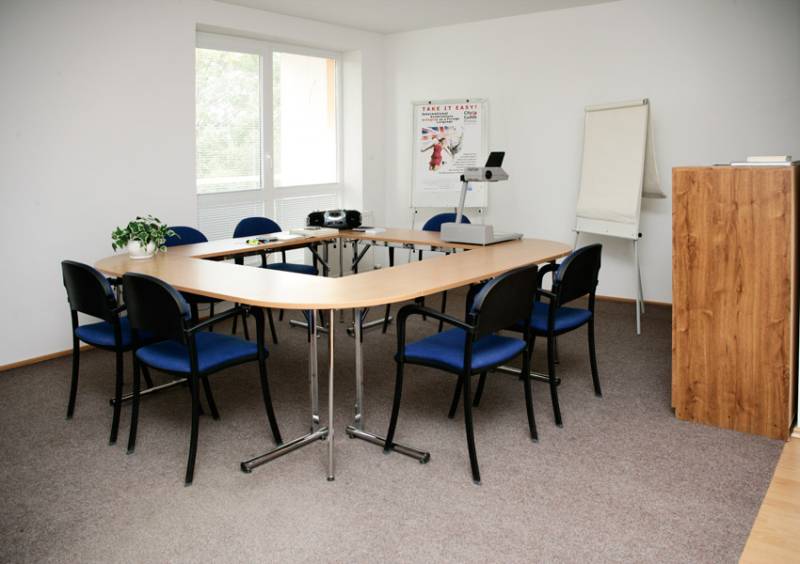 A meeting room with a dining table, blue chairs, a projector, and a screen in commercial premises.