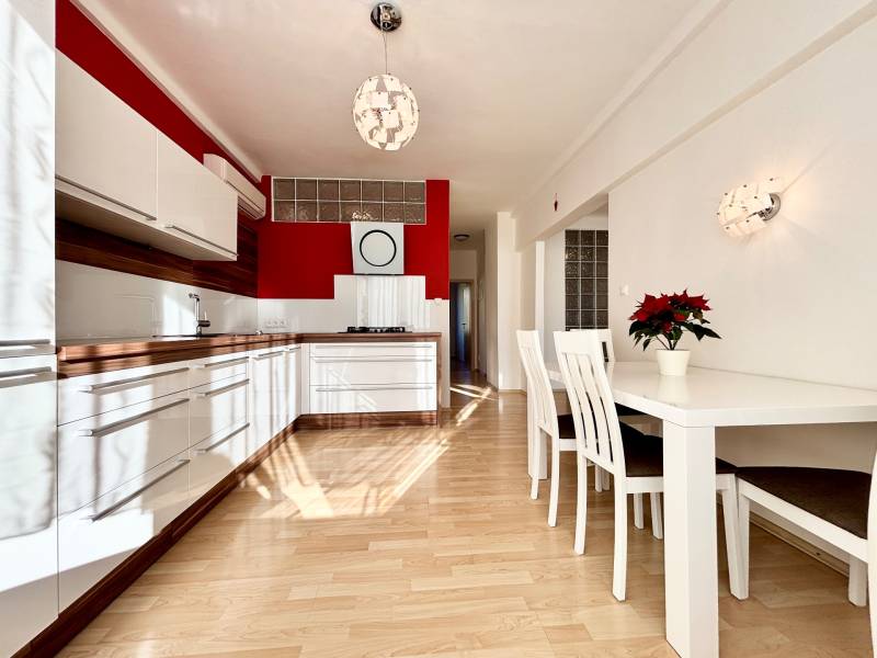 A kitchen in a 2-room apartment with white furniture and a wooden decor floor.