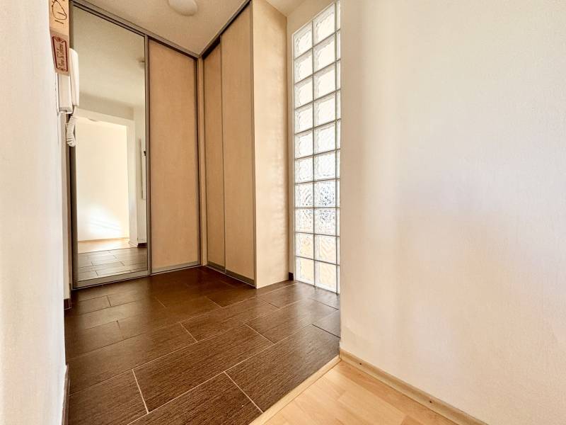Hallway of a 2-room apartment with a wooden decor floor, mirrored wardrobe, and glass wall.