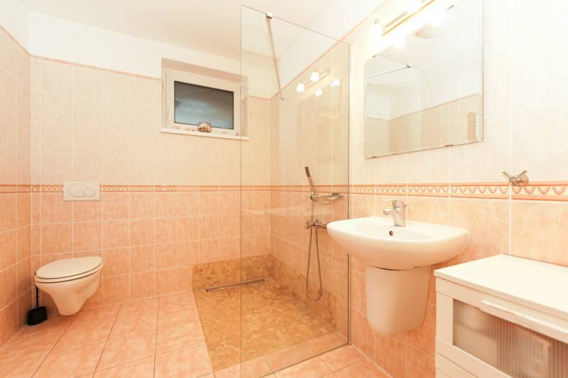 A bathroom in a family house with a toilet, shower, and sink on light tiles.