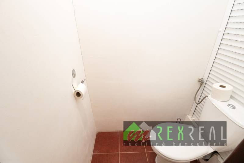 A toilet in a 4-room apartment with white walls and red tiles.