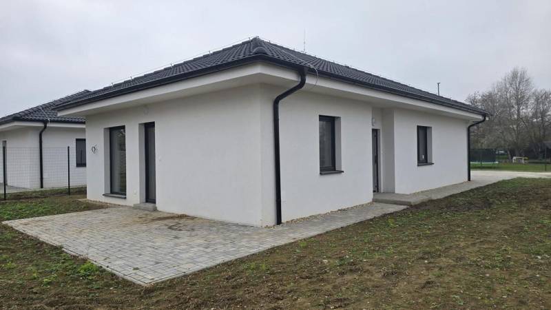 A family house in Cífer with a sloped roof and a paved terrace in the garden.