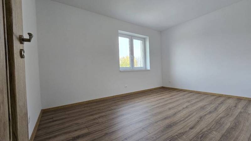An empty room in a family house with a wood-patterned floor and a window.