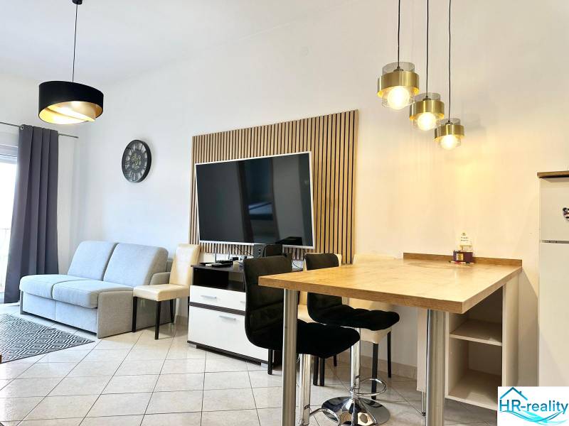 Living room of a holiday apartment with a TV, sofa, and bar seating.