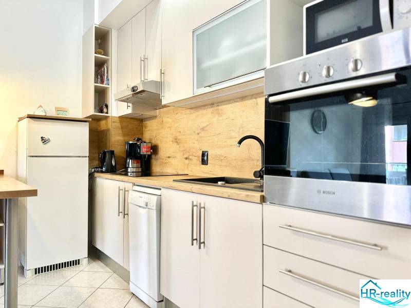 A kitchen in a vacation apartment with white furniture and wooden decor on the wall.