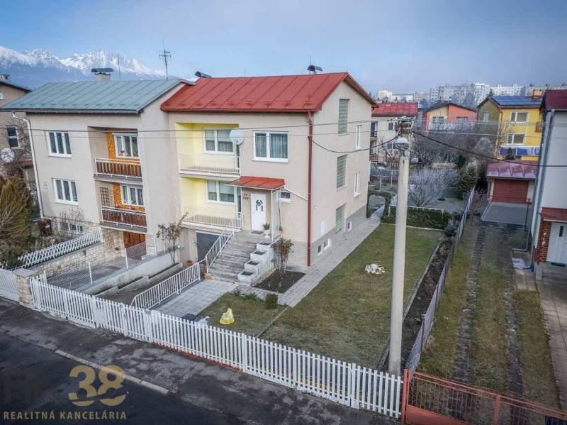 A family house in Poprad, with a colorful facade and a simple front garden, near apartment buildings.