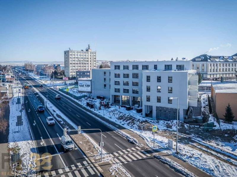 A building in Poprad by a busy road, snowy landscape, blue sky.