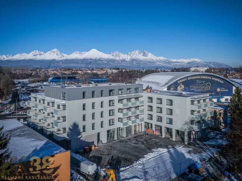 A building in Poprad with the snow-covered Tatras in the background and an ice rink.