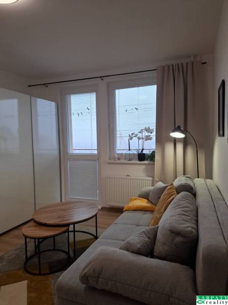 Studio apartment with a comfortable sofa, tables with wooden decor, and a window with curtains.