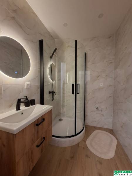 A studio apartment bathroom with a wooden decor floor and a modern shower enclosure.