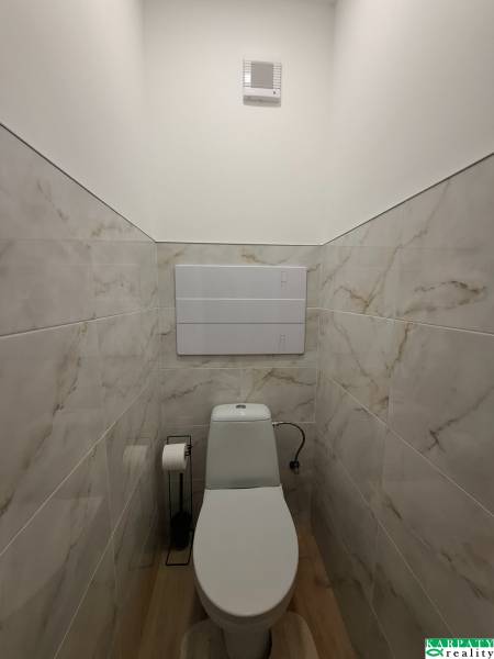 A toilet in a studio apartment with a wooden decor floor and marble-like tiles.
