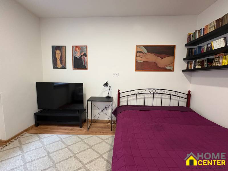 A bedroom in a studio apartment with a television and paintings on bare walls.