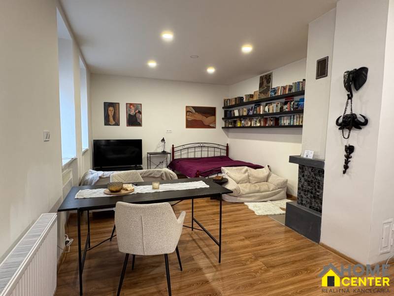 Interior of a 1-room apartment with a wooden floor, a bed, and a dining table.