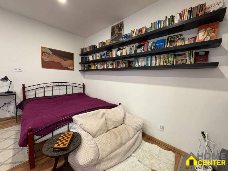 A studio apartment with a library, art on the wall, and a bed with a purple throw.