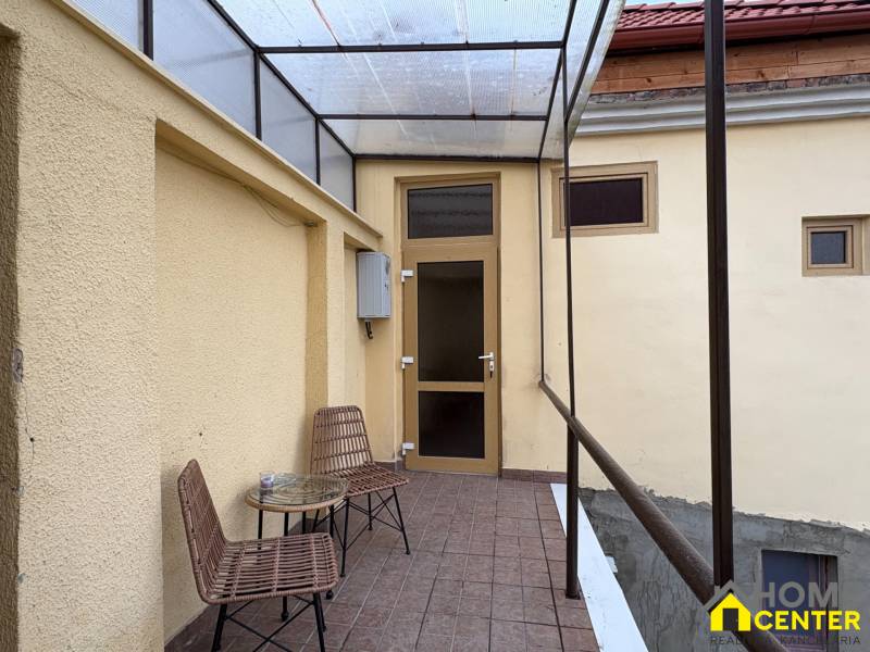 A covered patio with two chairs and a table in front of the entrance to a studio apartment.