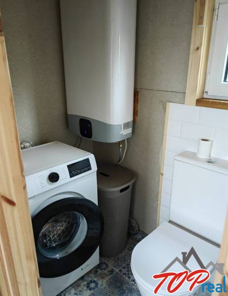 A bathroom in a family house with a washing machine, boiler, and toilet. The floor has decorative tiles.