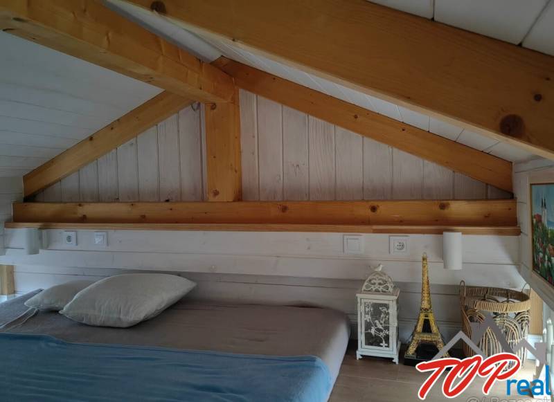 Attic bedroom in a family house with a wooden ceiling and decorations next to the bed.