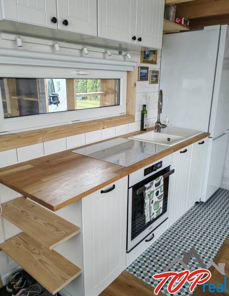 A kitchen in a family house with white cabinets, a wooden countertop, and patterned tiles.