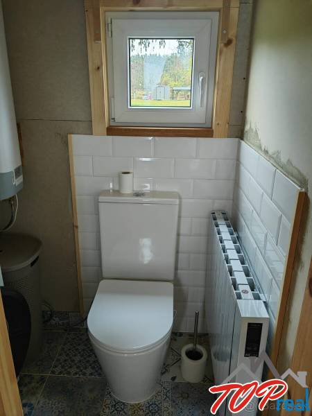 A toilet with white tiles and a view through a small window in a family house.