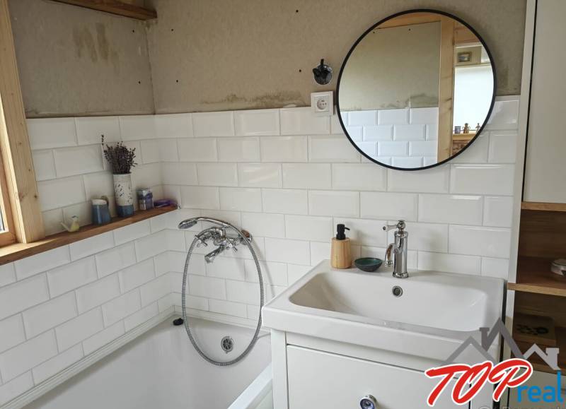 A bathroom in a family house with a bathtub, white tiles, and a round mirror.