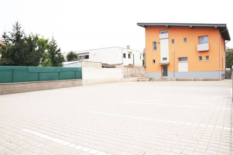 Orange building in Šaľa with a steep roof and a paved parking area.