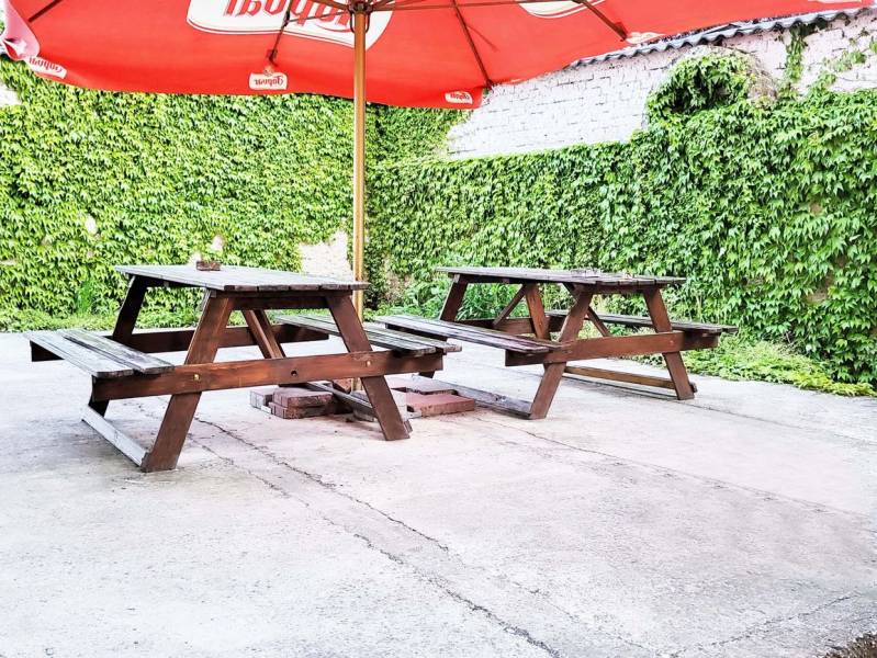Garden terrace in Šaľa with wooden tables and chairs under a red umbrella.