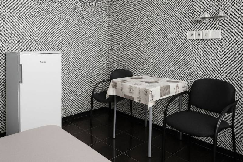 Interior with black and white patterned wallpaper, a standalone refrigerator, a table, and two chairs.