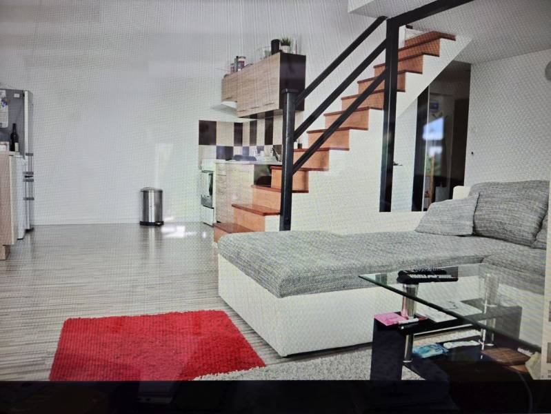 Living room with a kitchenette, staircase, sofa, glass table, and wooden decor flooring.