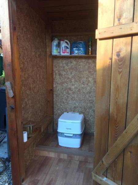 Wooden cabin in Kráľová nad Váhom with a chemical toilet and a shelf.