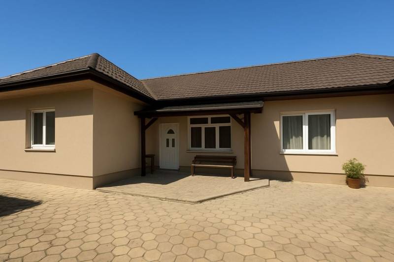 A family house in Tešedíkovo with a sloped roof, paving, and a wooden shelter.