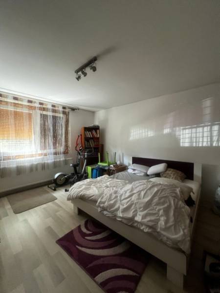 Bedroom with a bed, exercise machines, bookshelf, and wooden decor flooring in a family house.