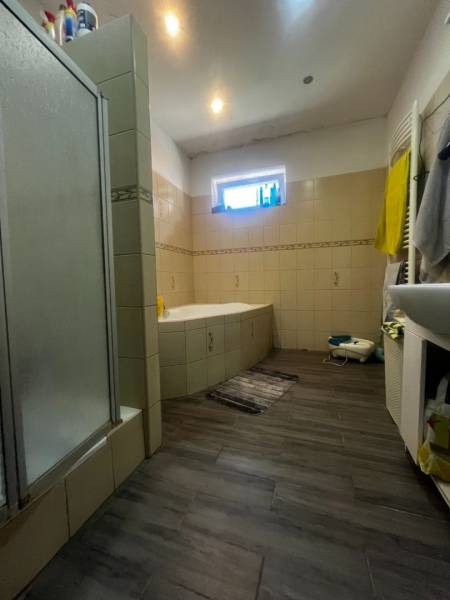 A bathroom in a family house with a bathtub, shower corner, and wooden floor decor.