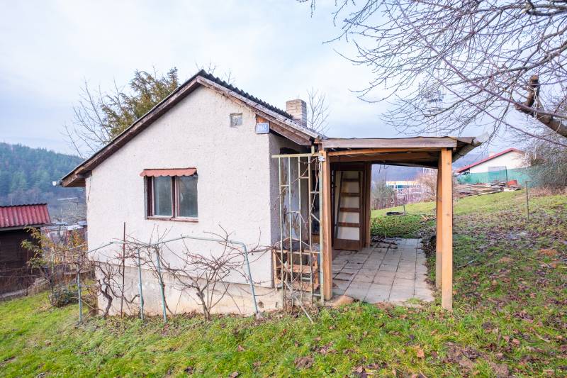 A cottage in Prešov with a wooden structure and a vineyard on a grassy hill.