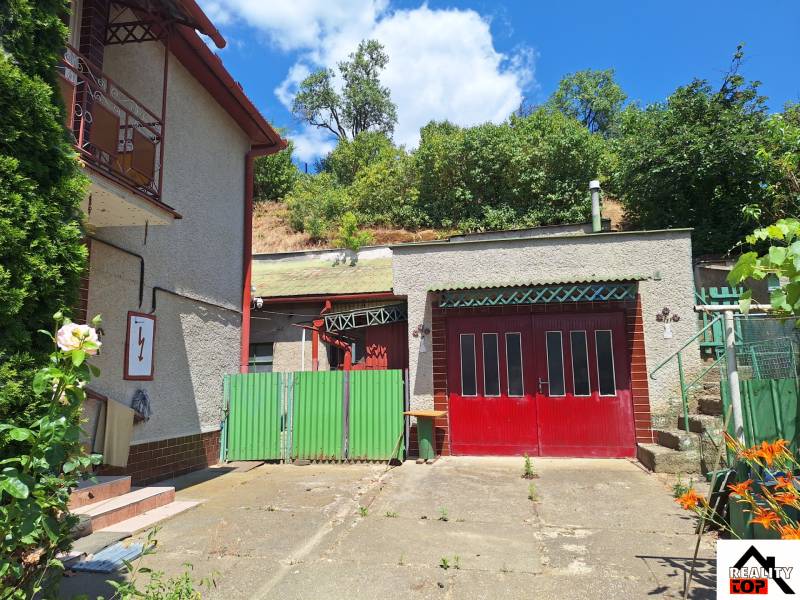 A family house in Tachtoch with an entrance gate, a garage, and surrounding greenery.