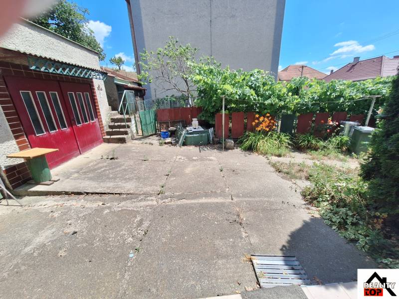 A family house in Tachtoch with a yard, concrete area, greenery, fence, and garage doors.