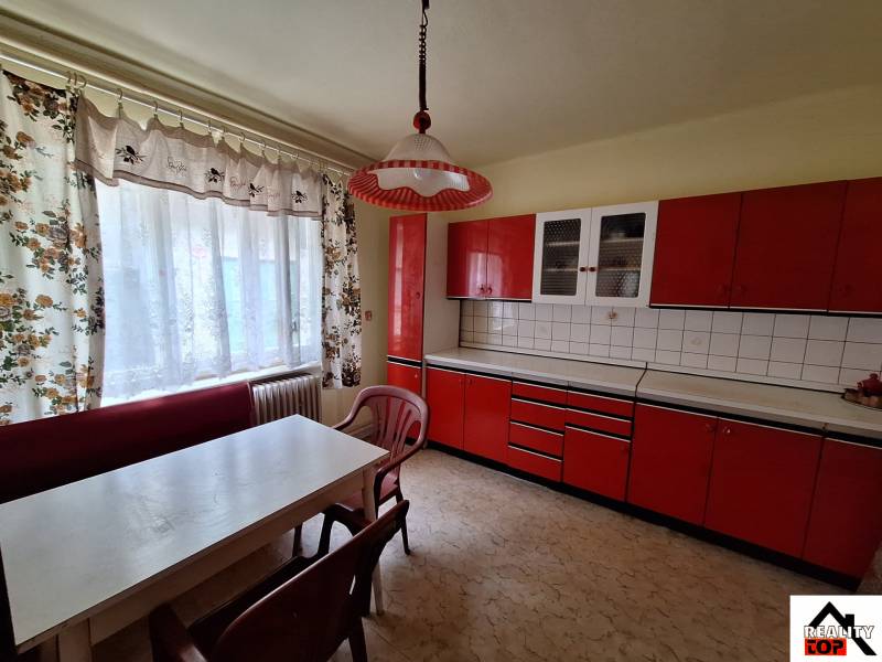 A kitchen in a family house with red kitchen cabinets and white curtains.