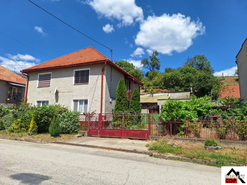 A family house in Tachtoch, with a red roof, fence, and garden in a green environment.