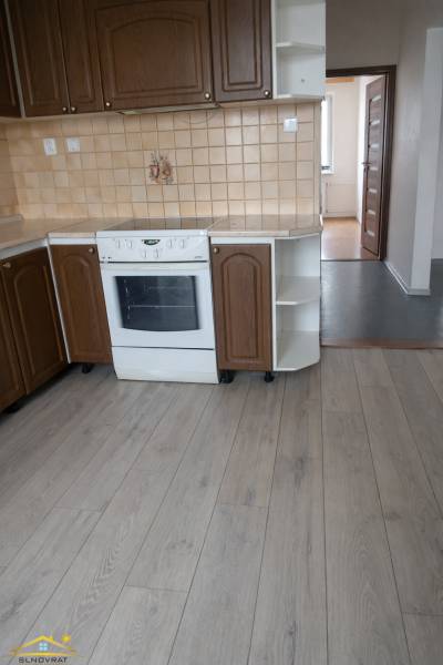 A kitchen with brown cabinets, a white stove, and a floor with a wood design, in a three-room apartment.